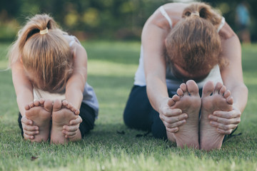 Mother and daughter doing yoga exercises on grass in the park at