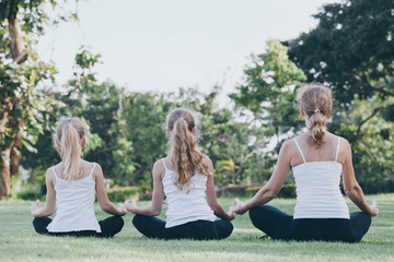 Mother and daughter doing yoga exercises on grass in the park at