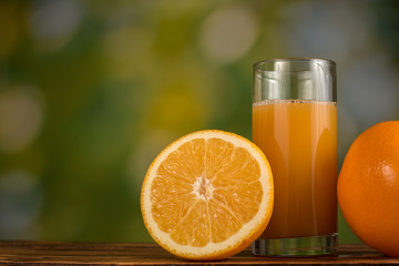 Orange juice in glass and oranges on natural green background