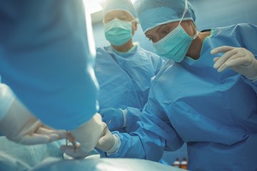 Team of surgeons performing operation in operation theater - obrazy, fototapety, plakaty