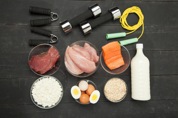 Proteins and dumbbells. Fish, cheese, eggs, meat, chicken  heart on a black wooden background