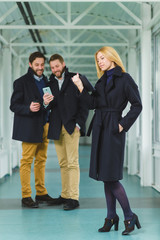 Blond businesswoman holding smart phone in lobby with colleagues at background