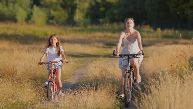 Young woman riding with girl on bicycles in the filed at sunset