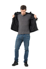 Fototapeta premium Casual man in jeans taking off leather jacket looking down. Full body length portrait isolated over white background.