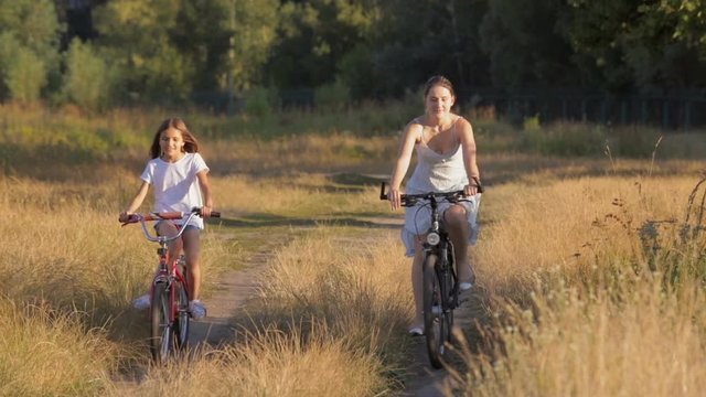 Beautiful young woman with girl riding bicycles in field at countryside