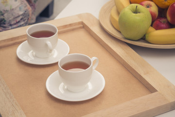 Toned picture of two cups of tea represented on wooden tray. Tea set for two persons. Bowl with different fruits represented near by.