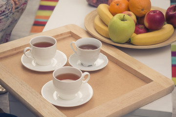 Tea set for three persons. Toned picture of three cups of tea represented on wooden tray. Bowl with different fruits represented near by.