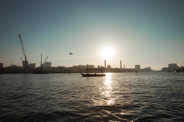 Obraz premium silhouette of a boat floats on the sea channel of Dubai on the background of the setting sun, the long-range plan, Dubai