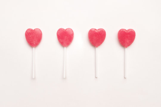 four Pink Valentine's day heart shape lollipop candy arrange on empty white paper background. Love Concept. Knolling top view. Minimalism colorful hipster style.