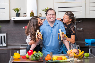 Two young women are fed bananas midle age man in the kitchen