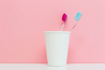 pink and blue toothbrushes in the white cup in the bathroom on a pink background