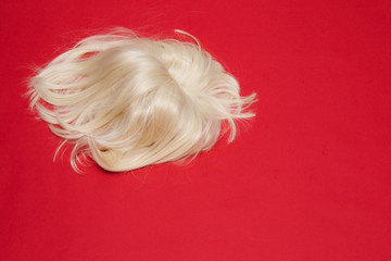 the blonde wig fell on red background. the concept for barbershop.