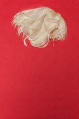 fashion blonde wig on a red background. minimalism. flat lay.