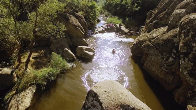 Male jumping from rock to the river where people swiming bathing with husky dog. Drone footage