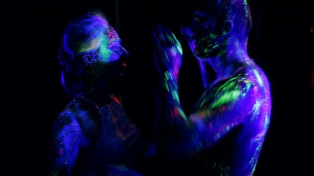 Couple in love painted fluorescent powder dance in ultraviolet light