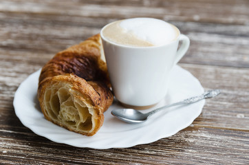 Coffee cup with milk and fresh baked croissants wooden background. Traditional breakfast concept.