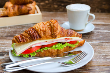Freshly croissant with ham, cheese and salad  on wooden background. Breakfast concept.