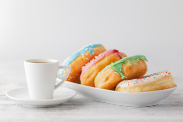 Few colorfull donuts lay on plate with cup of espresso