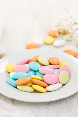 color candies on white plate on wooden background