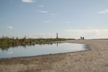 low angle shot of people walking on path amidst fields at german north sea coast on sunny day with lighthouse in distant background