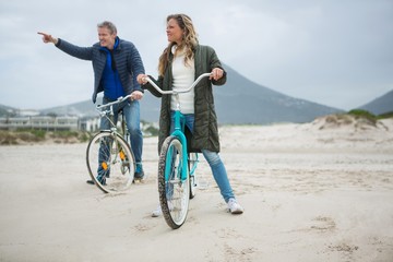 Couple on bicycle pointing at distance on beach