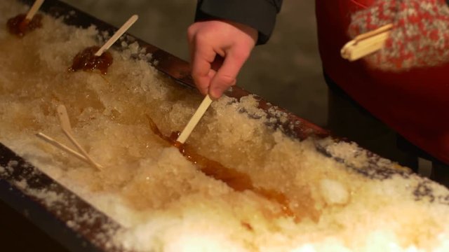 man prepares maple syrup on stick in ice-Canadian treat
