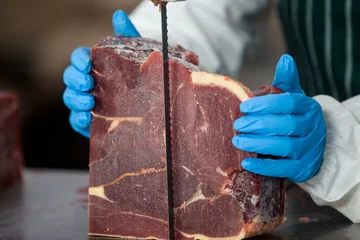 Crédence de cuisine en verre imprimé Viande Boucher femelle coupant la viande crue sur une scie à ruban