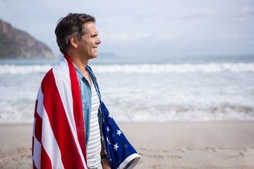 Man wrapped in amrican flag standing on beach