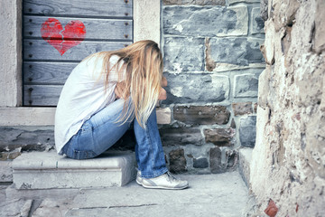 Unhappy woman with broken heart sits outside on the stone stairs in the city street.