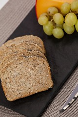 Slices of brown bread, grapes and gouda cheese on slate board