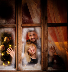 happy cheerful man and woman looking through the frozen window