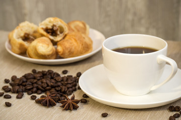 White cup of coffee and croissants with coffee beans scattered on the table