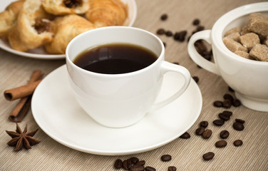 White cup of coffee and a croissant with coffee. On the table there are coffee beans, cinnamon and star anise