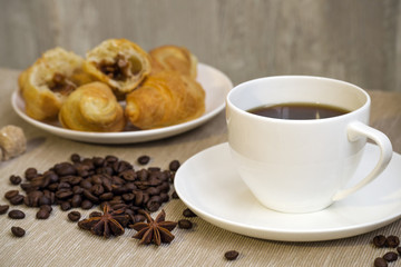 White cup of coffee and croissants with coffee beans scattered on the table
