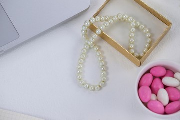 Close-up of pearl necklace, pebbles and laptop