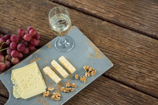 Pieces of cheese, walnut, grapes and glass of wine on tray