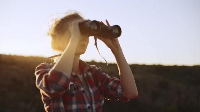 Blonde Caucasian female in plaid red shirt using binoculars to look forward in slowmotion