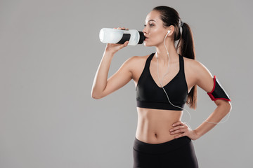 Young fitness lady drinking water over grey background
