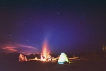 Camping fire under the amazing blue starry sky with a lot of shining stars and clouds. Travel recreational outdoor activity concept.