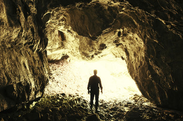 Cave exploring. Man silhouette at cave entrance with sunlight entering the dark cave tunnel,...