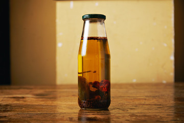 Gourmet olive oil with chilli and black pepper in a small glass bottle with colored metal cap in a rustic kitchen