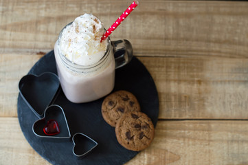 Portion of hot chocolate with whipped cream topping and red straw served on black slate board with chocolate cookies and hearts. Love and romantic concept. St. Valentine Day