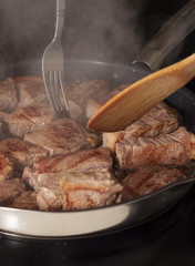 Close up of turning beef fillet steaks with a fork and a wooden spatula.
