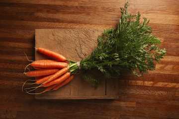 A bunch of fresh carrots on a weathered old cutting board with deep cuts on a beautiful wooden...