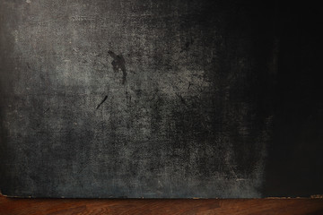 Texture of an old heavily used black dark gray slate chalkboard board presented over wooden table