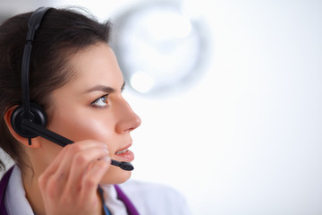 Doctor wearing headset sitting behind a desk with laptop over grey background