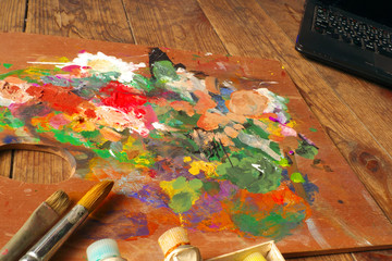 Palette and paintbrushes with notebook computer on wood background