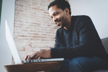 Cheerful African man using computer and smiling while sitting on the sofa.Concept of young business people working at home.Blurred background.