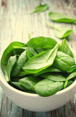 Fresh Baby spinach leaves in white bowl on blue wooden background. Top view with copy space,...