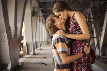 Young couple kissing in the summer daylight on a bridge construc